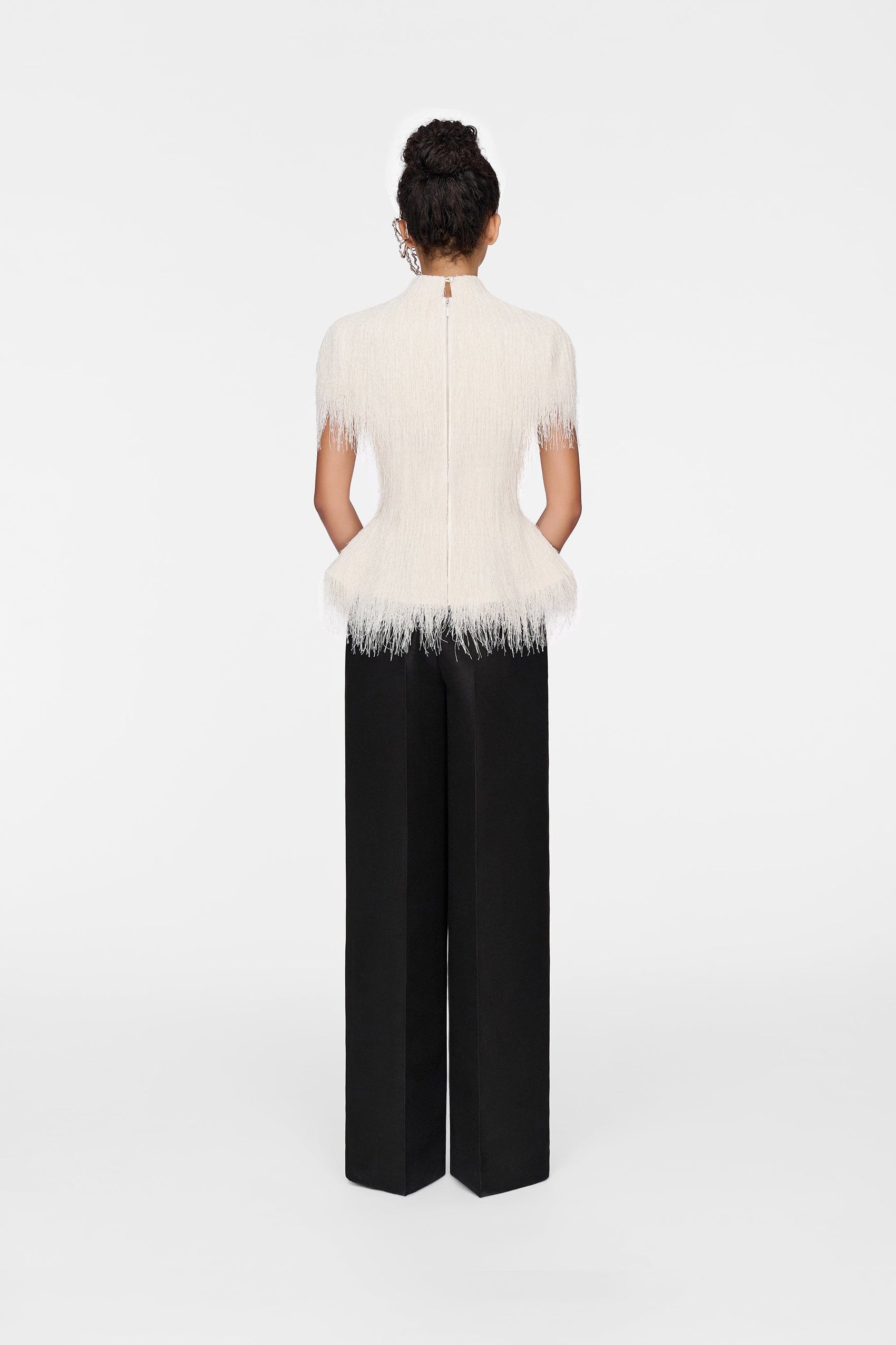 Woman in feathered top & black pants, back view